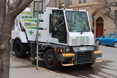 Electric street sweeper next to a sidewalk.